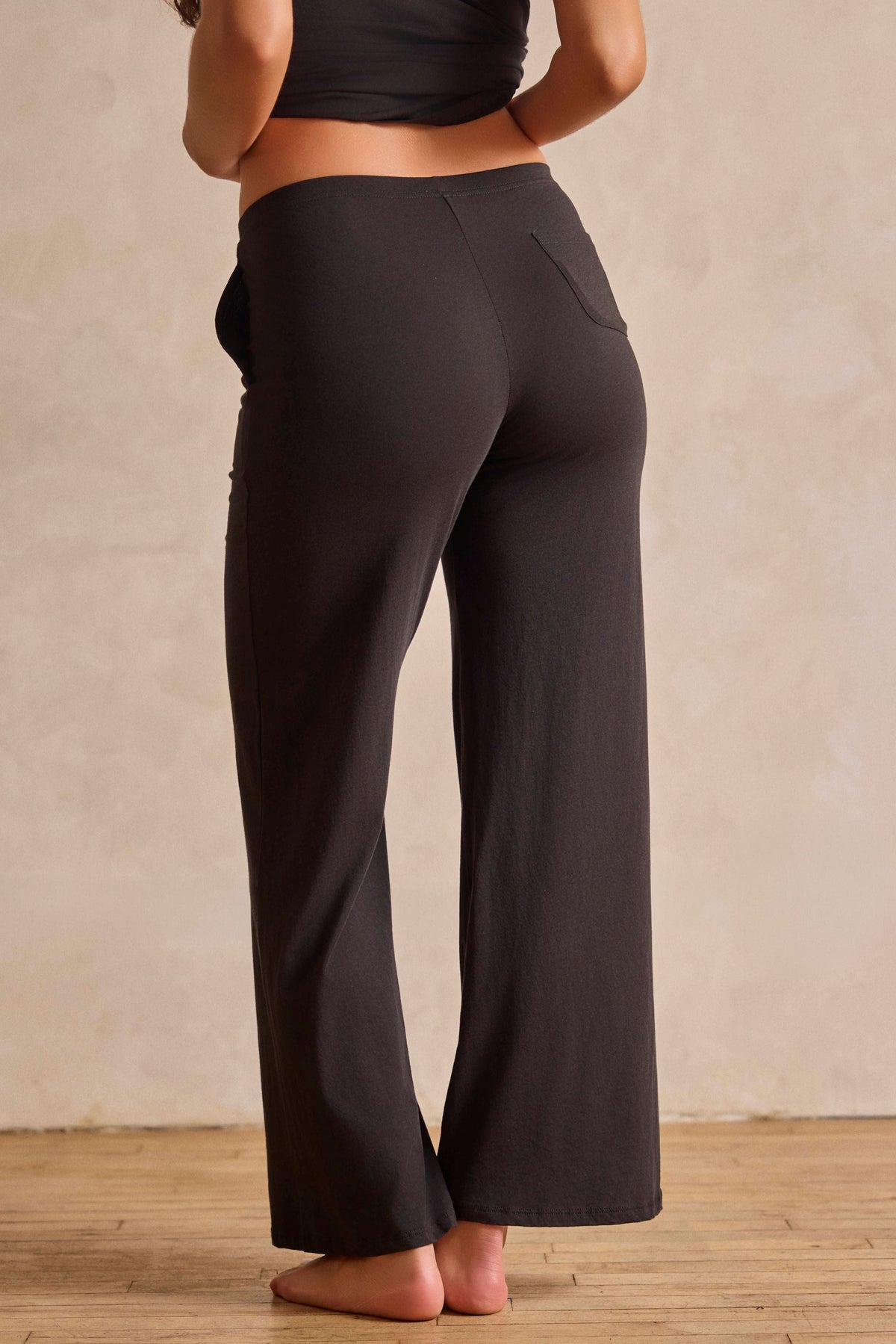 A woman shown from the back wearing black wide-leg cropped pants and a black camisole top