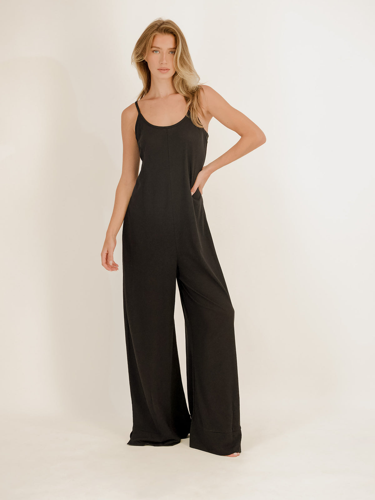 A woman modeling a black sleeveless wide-leg jumpsuit against a plain white studio background.